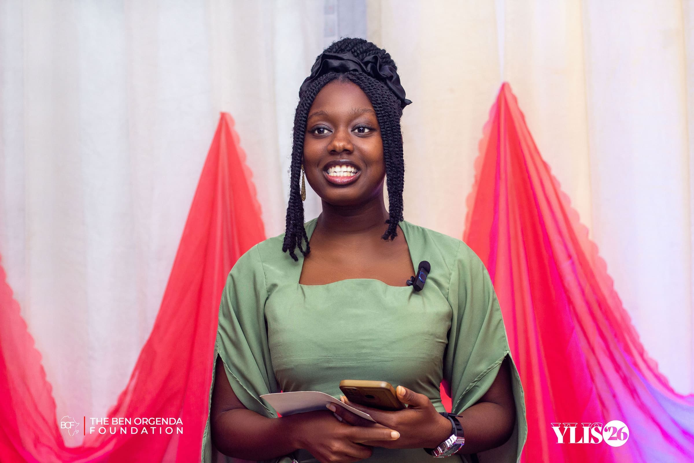The host smiling on stage at YLIS 2026, holding the programme and a phone